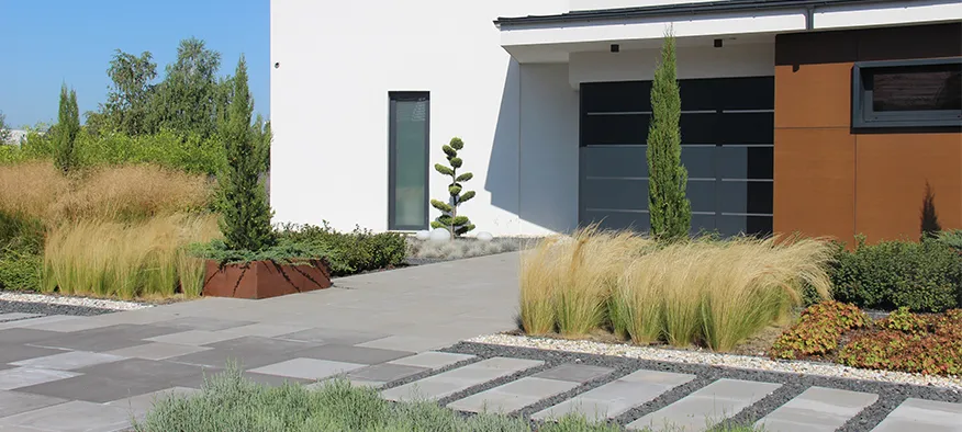 Front garden of a modern house with ornamental grasses, columnar evergreens and stone paving